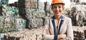Femme en casque orange supervisant la gestion des déchets plastiques devant une pile de bouteilles en plastique.