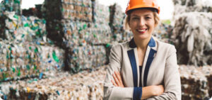 Donna con cappello rigido arancione che supervisiona la gestione dei rottami di plastica davanti a una pila di bottiglie di plastica.